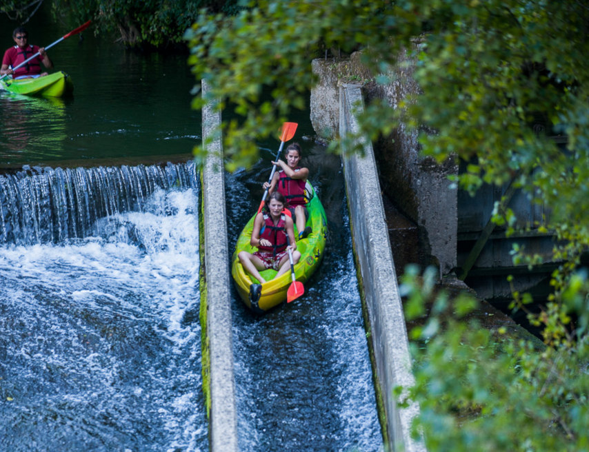 Canoë biplace franchissant la glissière d’un seuil sur l’Aveyron, deux jeunes en gilet de sauvetage